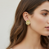 Close-up of a woman wearing a gold earring with a white stone on a neutral background