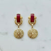 Gold earrings with red stones on a marble background