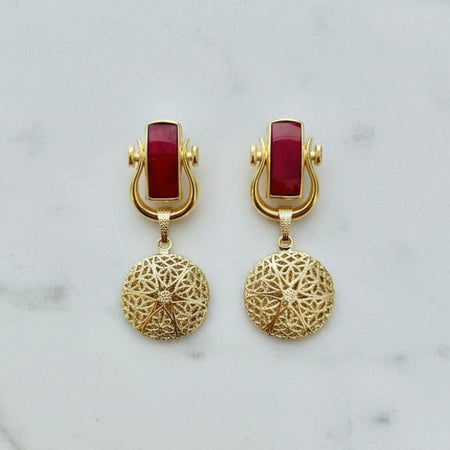 Gold earrings with red stones on a marble background