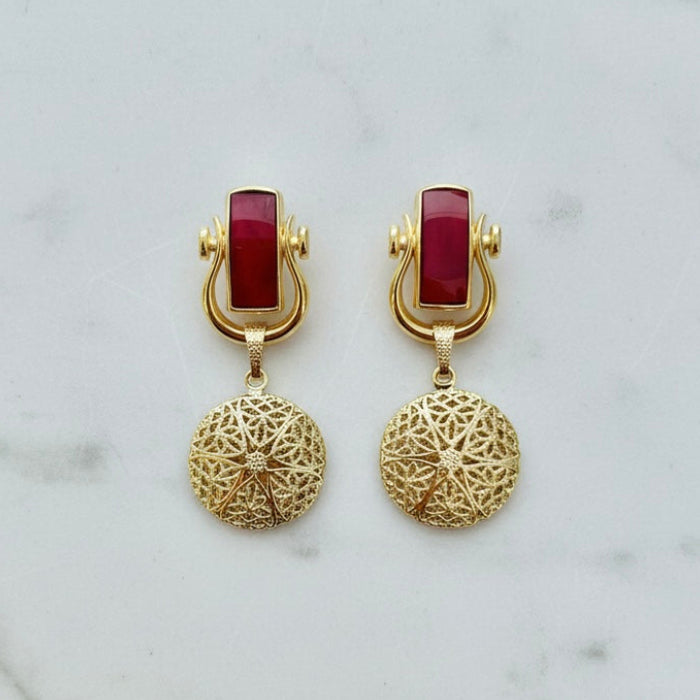 Gold earrings with red stones on a marble background