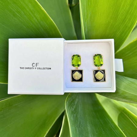 Green gemstone earrings in a white box with 'The Christy F Collection' branding, set against a green leafy background.