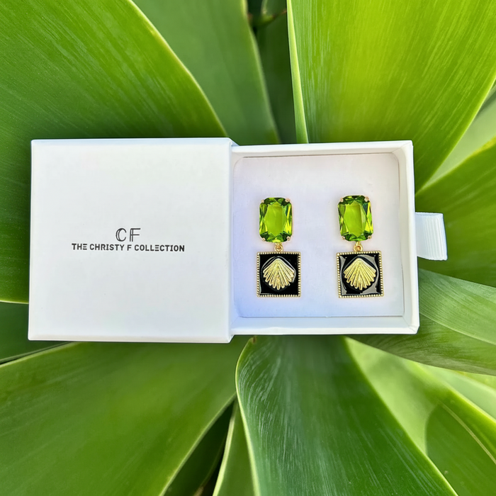 Green gemstone earrings in a white box with 'The Christy F Collection' branding, set against a green leafy background.