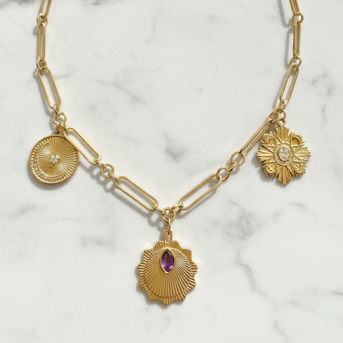 Gold necklace with three charms on a marble background