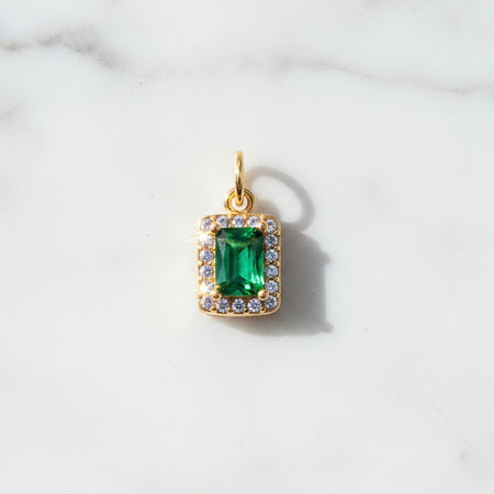 Gold pendant with a green gemstone on a white marble background