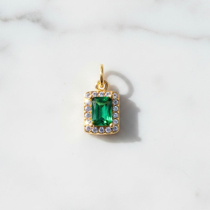 Gold pendant with a green gemstone on a white marble background