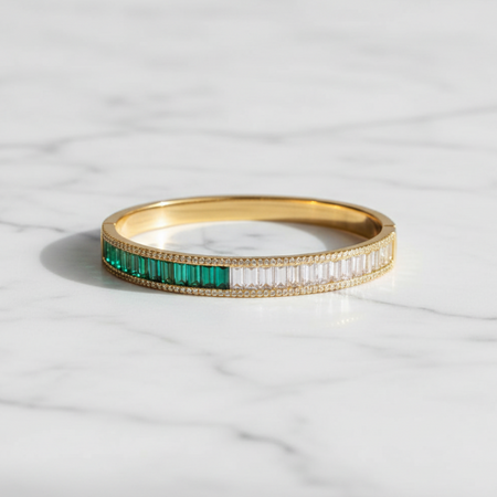 Gold bracelet with green gemstones on a marble surface
