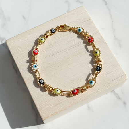 Gold bracelet with colorful eye-shaped beads on a wooden block