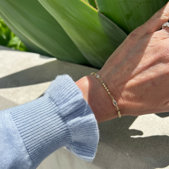 Hand wearing a gold bracelet with a plant in the background