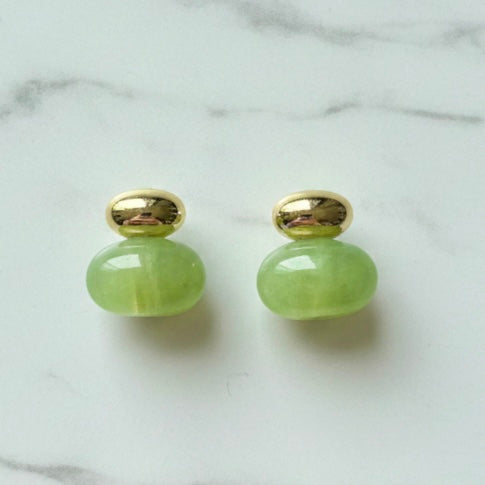 Pair of green earrings with gold tops on a marble surface