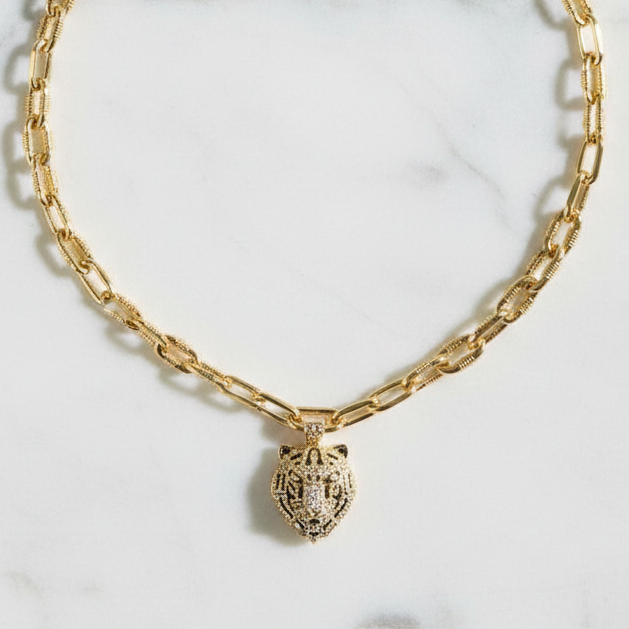 Gold chain necklace with a lion head pendant on a light gray background