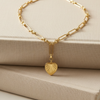 Gold necklace with a heart-shaped pendant on a beige fabric background