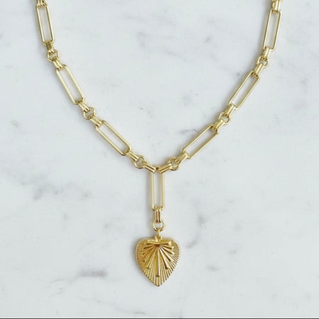 Gold necklace with a heart-shaped pendant on a marble background
