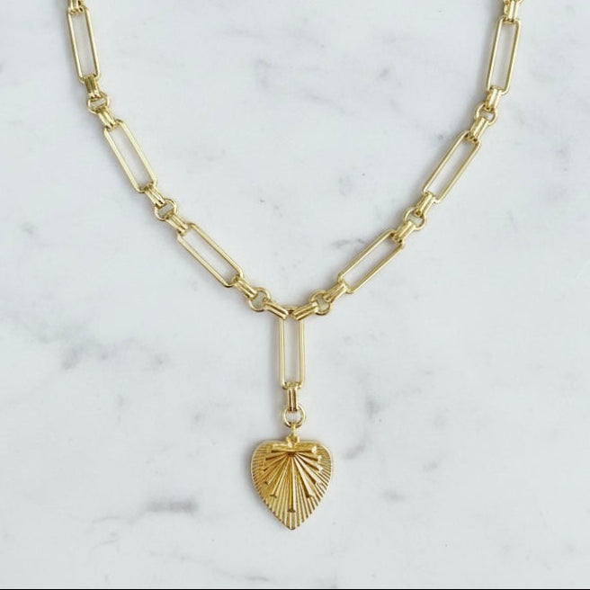 Gold necklace with a heart-shaped pendant on a marble background