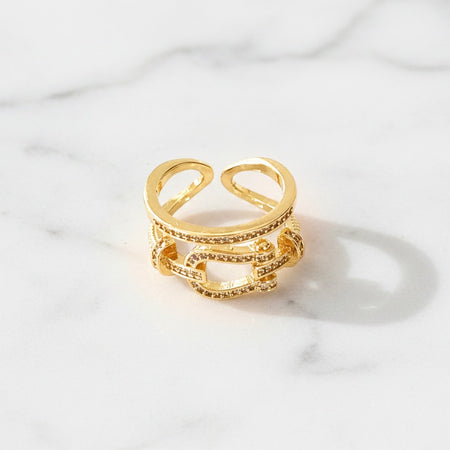 Gold ring with intricate design on a light marble background