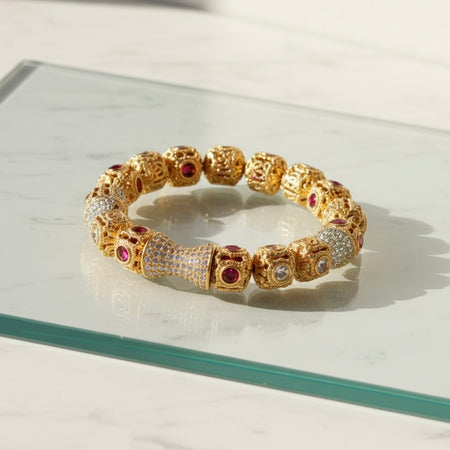 Gold bracelet with embedded gemstones on a reflective surface