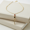 Gold necklace with a cross pendant and red gemstone on a white surface