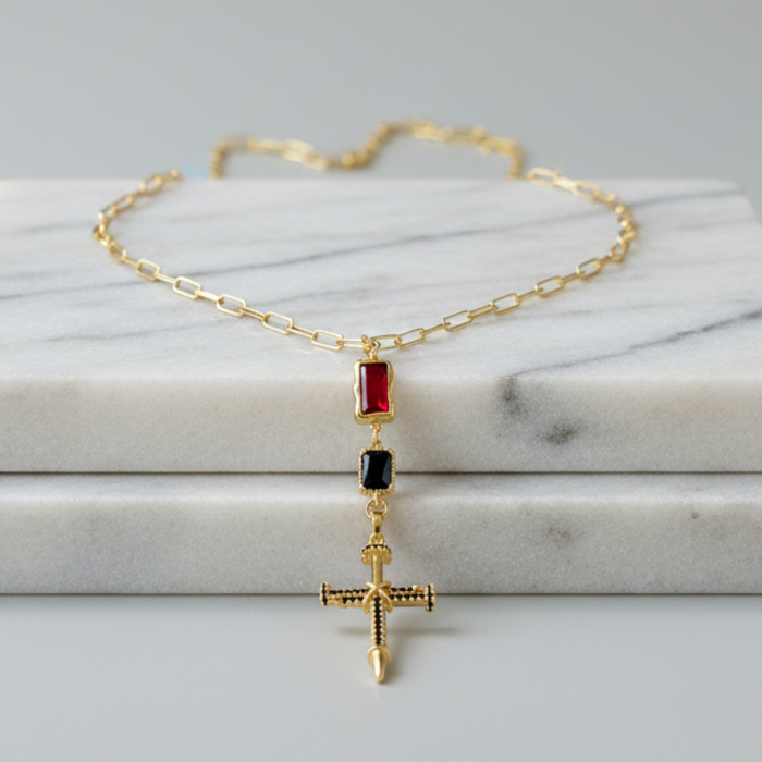 Gold necklace with red and black gemstones on a marble surface