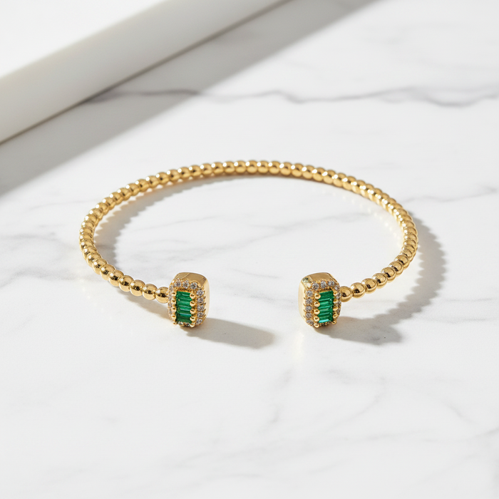 Gold bracelet with green gemstones on a white surface