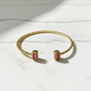 Gold bracelet and earrings with pink gemstones on a white fabric background