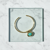 Gold bracelet with a turquoise stone on a marble surface