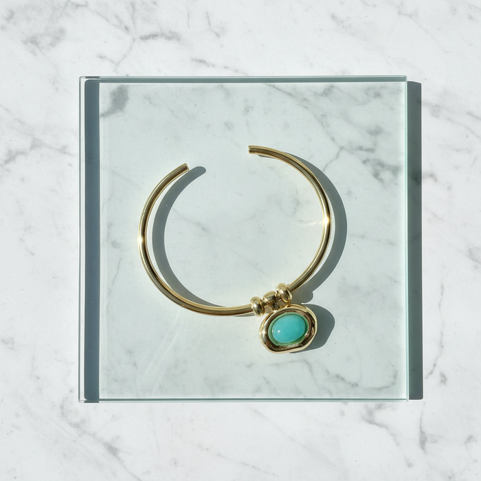 Gold bracelet with a turquoise stone on a marble surface