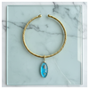 Gold necklace with a blue pendant on a marble surface