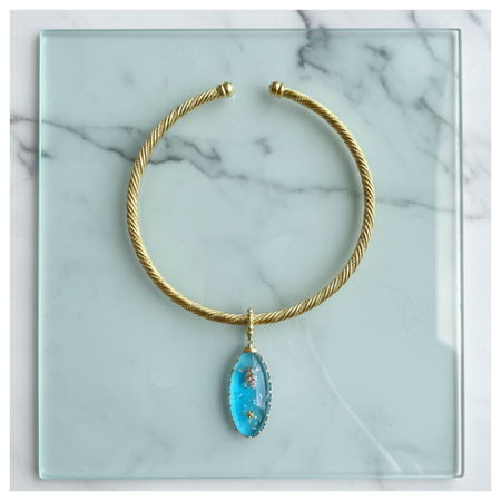 Gold necklace with a blue pendant on a marble surface