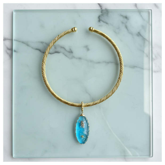 Gold necklace with a blue pendant on a marble surface