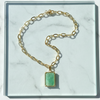 Gold chain bracelet with a green gemstone on a marble surface