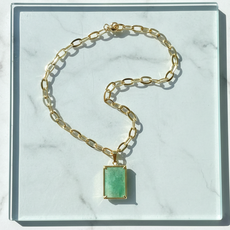 Gold chain bracelet with a green gemstone on a marble surface