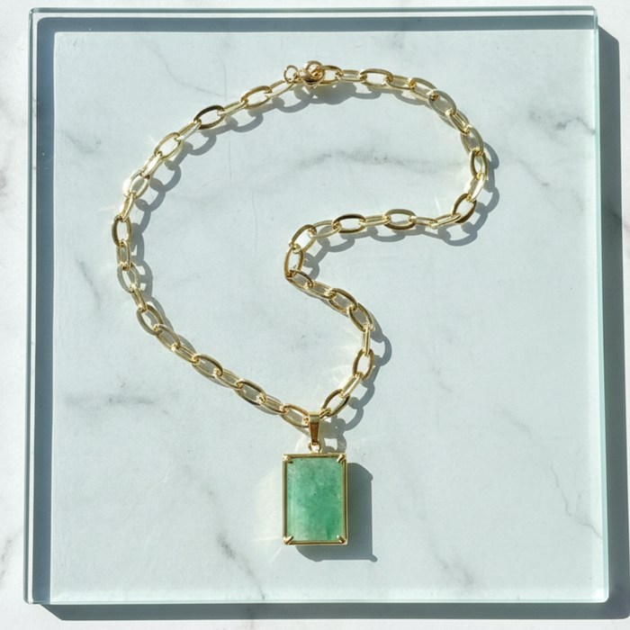 Gold chain bracelet with a green gemstone on a marble surface