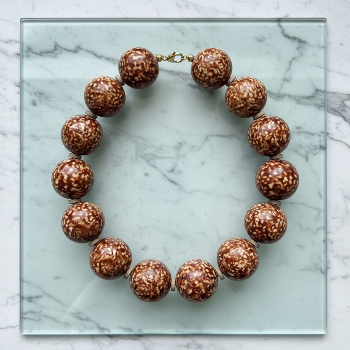 Brown beaded necklace on a glass surface with a marble background