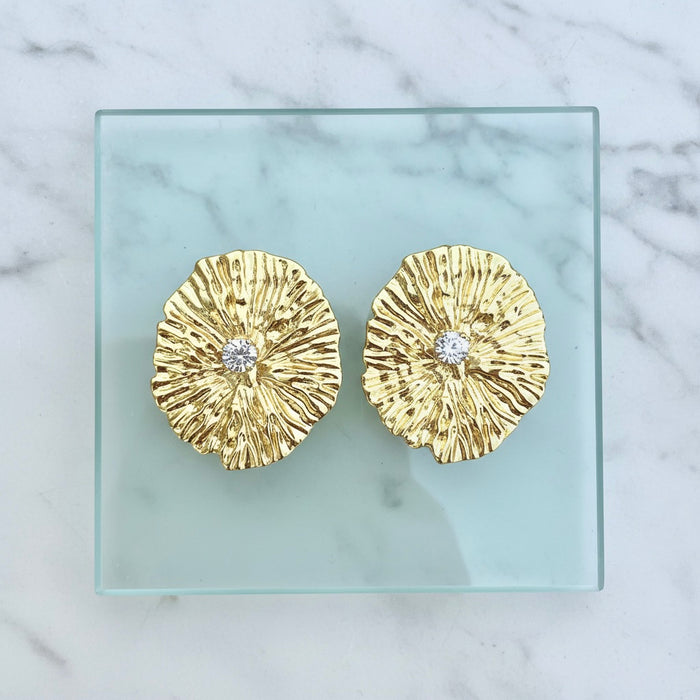 Gold earrings with diamond centers on a clear glass plate against a marble background