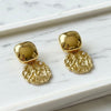 Gold earrings with textured designs on a marble surface