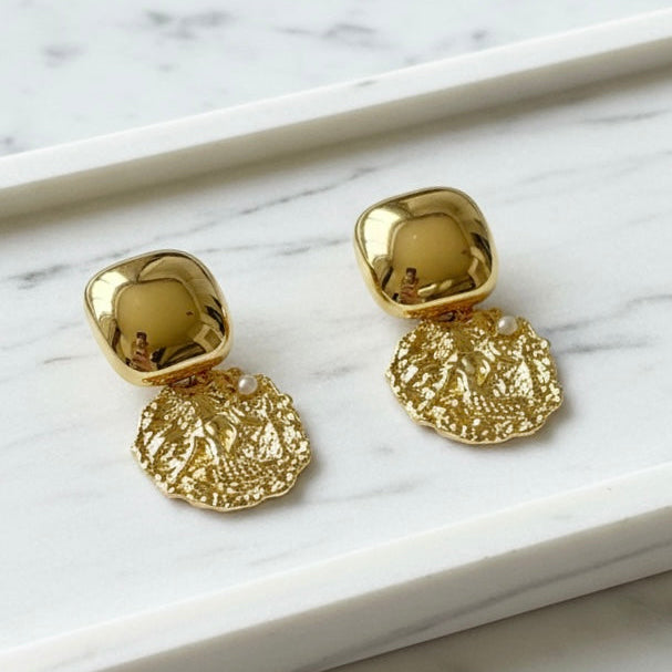 Gold earrings with textured designs on a marble surface