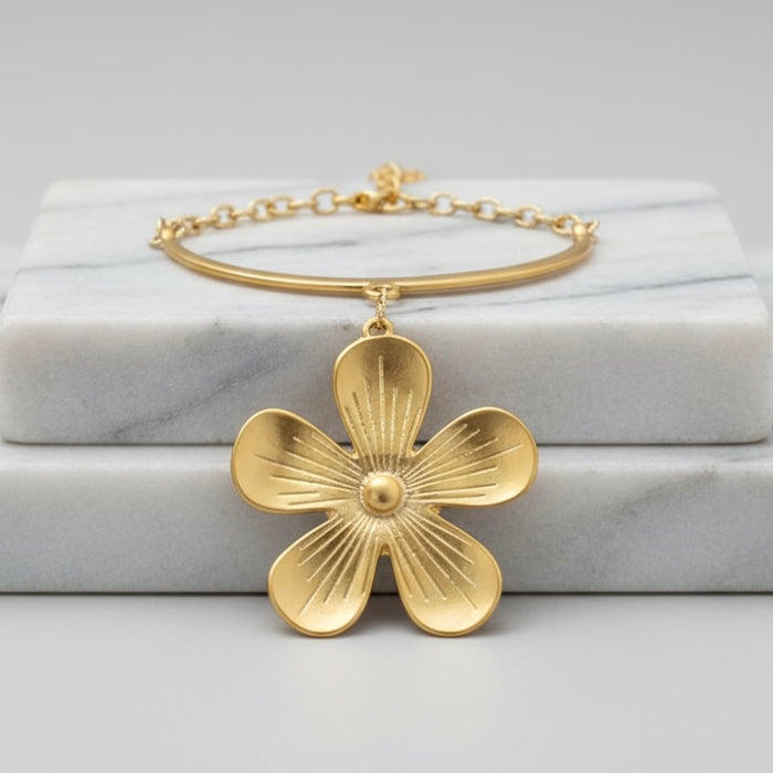 Gold NECKLACE with a floral pendant on a marble surface