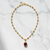 Gold necklace with a red gemstone pendant on a marble background