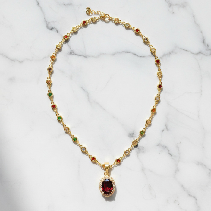 Gold necklace with a red gemstone pendant on a marble background