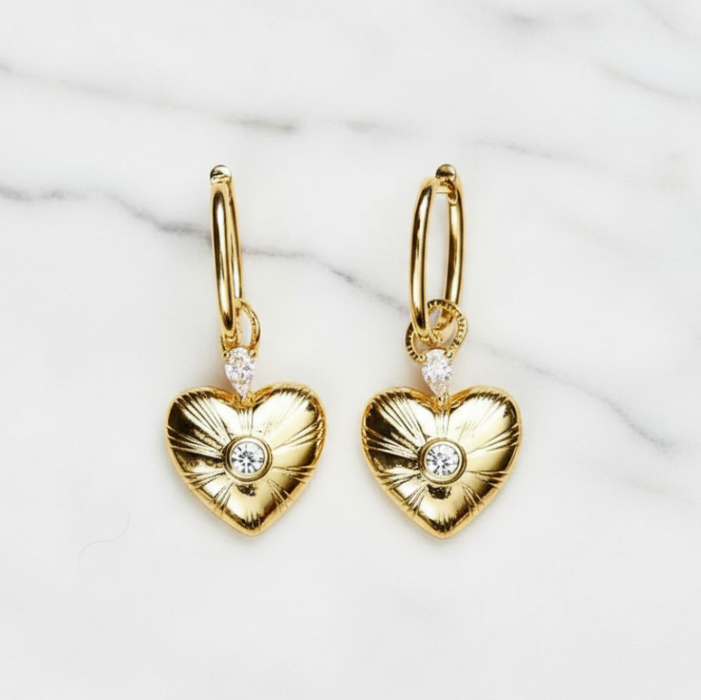 Gold heart-shaped earrings with diamond accents on a white marble background
