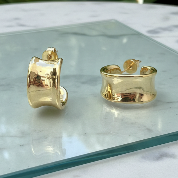 Gold hoop earrings on a glass surface with a marble background