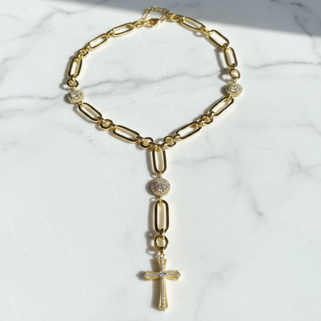 Gold chain necklace with a cross pendant on a marble surface