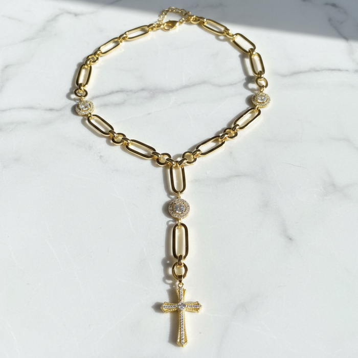 Gold chain necklace with a cross pendant on a marble surface