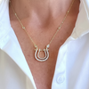 Gold necklace with a horseshoe pendant on a person wearing a white shirt.