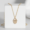 Gold necklace with a hamsa hand pendant on a white stand against a gray background