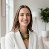 Woman in a white blazer sitting in a modern room with plants and furniture wearing a green beaded necklace with a gold spacer bead.