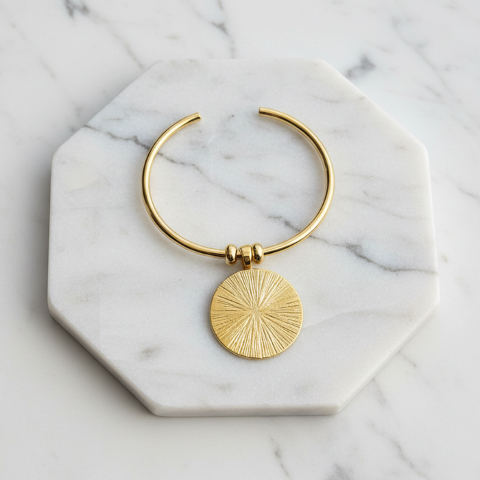 Gold bracelet with a circular pendant on a marble surface