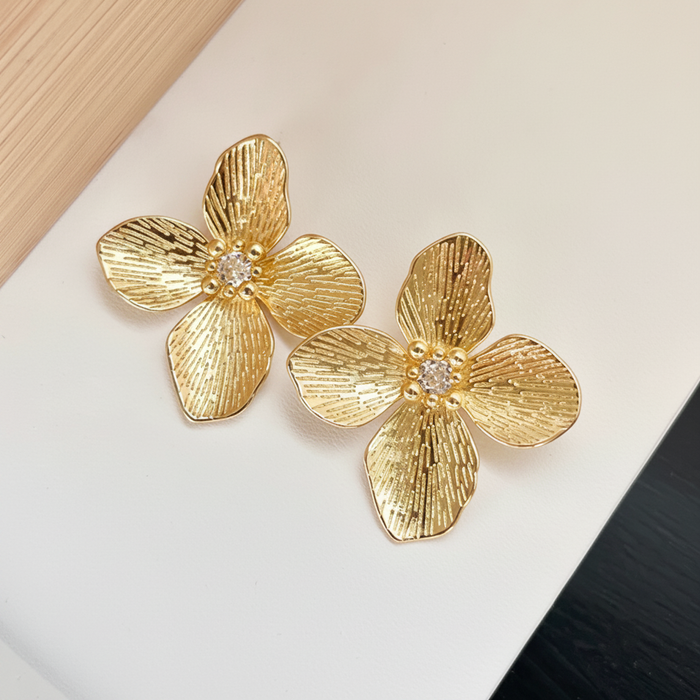 Gold flower-shaped earrings with a central gemstone on a light background