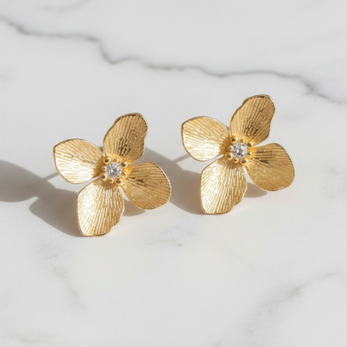 Gold flower-shaped earrings on a marble surface