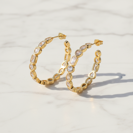 Gold hoop earrings with embedded stones on a light background