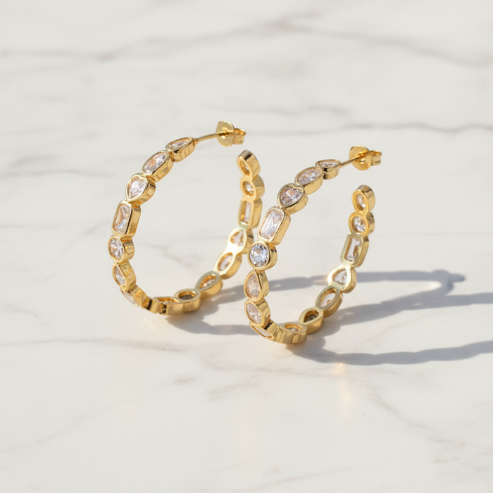 Gold hoop earrings with embedded stones on a light background